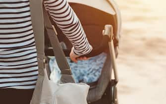 Mother walking with baby in a stroller on bright sunny spring day