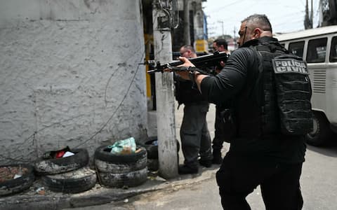 Police officers take cover during the Operacao Contencao (Operation Containment) at the Vila Cruzeiro favela, in the Penha complex, in Rio de Janeiro, Brazil, on October 28, 2025. At least 2,500 agents took part in an operation to arrest drug traffickers from the Comando Vermelho (CV), which resulted in, at least, 18 suspects and several police officers dead. (Photo by Mauro PIMENTEL / AFP)