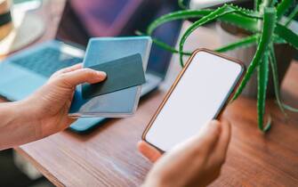 A woman holds passport, credit card and phone with white screen in her hands. Online travel booking using computer. Business trip planning