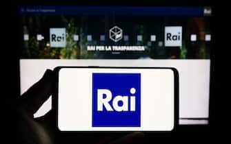 Person holding smartphone with logo of company RAI – Radiotelevisione Italiana S.p.A. on screen in front of website. Focus on phone display.