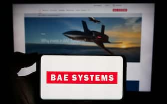 Person holding smartphone with logo of British aerospace and defense company BAE Systems plc in front of website. Focus on phone display.