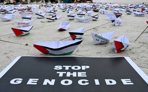 A flotilla of paper boats are laid on the ground near a poster reading "Stop the Genocide" during a demonstration in support of Gaza and Palestinian people at Venice Lido during the 82nd Venice International Film Festival, on August 30, 2025. (Photo by Stefano RELLANDINI / AFP)