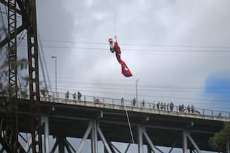 epa11035001 Hector Chacon, of the Municipal Firefighters, wears a Santa Claus costume as he descends from the Las Vacas railway bridge in Guatemala City, Guatemala, 17 December 2023, during a Christmas gift-giving ceremony to low-income children of the Jesus de la Esperanza settlement.  EPA/EDWIN BERCIAN