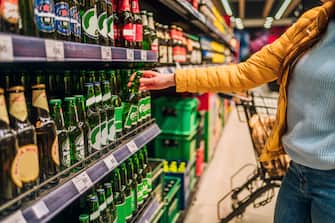 Woman customer in alcohol section in supermarket or liquor store holding a bottle from the shelf