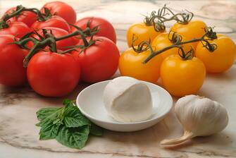 Close-up of red and yellow tomatoes on a marble table top, next to a bulb of garlic, several basil leaves, and a bowl of mozzarella cheese, 2009. (Photo by Tom Kelley/Getty Images)