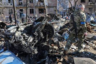 epa09833928 An armed man passes near a destroyed car near a building damaged by shelling in Kyiv as Russia's attack on Ukraine continues, Kyiv, Ukraine, 18 March 2022. On 24 February Russian troops had entered Ukrainian territory in what the Russian president declared a 'special military operation', resulting in fighting and destruction in the country, a huge flow of refugees, and multiple sanctions against Russia.  EPA/MIGUEL A. LOPES