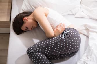 Elevated View Of A Woman Lying On Bed Having Stomach Pain