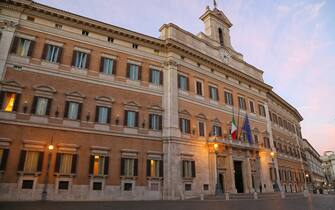 Italy, Roma. Evening view of the Italian Parliament building and the Chamber of Deputies with the Italian and European flag waving and the street lamps lit.