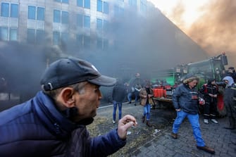 epa11117876 A protester reacts amidst smoke during a farmers' protest in front of the European Parliament on the sidelines of a EU summit in Brussels, Belgium, 01 February 2024. Several hundred tractors are expected to converge on Brussels on the sidelines of a European leaders' summit on 01 February, the Walloon Federation of Agriculture (FWA) announced. Farmers are protesting to highlight their declining incomes, overly complex legislation and administrative overload. The discontent among farmers, initially sparked in France, has spilled over into several European countries, including Belgium, particularly in the Walloon region.  EPA/OLIVIER MATTHYS