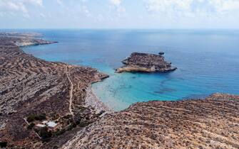 Aerial drone. Spiaggia and Isola dei Conigli, Lampedusa. 
Tranquil, cove-style beach with white sand and turquoise surf bordered by rocky cliffs.
