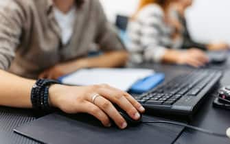 Close-up of a young man's hand on a computer mouse in a programing class