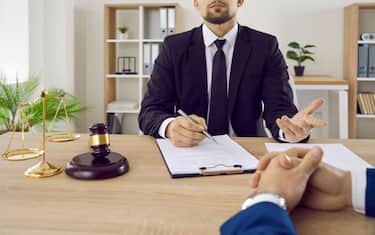 Lawyer, notary or judge consults and discusses contract documents with business client in office.