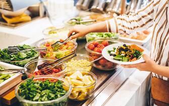 Woman choosing food for breakfast at hotel restaurant. Woman taking food from a buffet line.