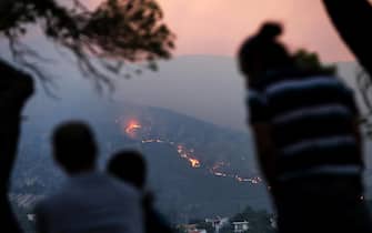 epa11546313 Residents watch the fire at Penteli mount, northeast Attica, Greece, 12 August 2024. Despite efforts by civil protection forces throughout the night, the fire raging in northeast Attica had advanced rapidly and was moving in the direction of Penteli, having spread over the Penteli mountain range. Authorities evacuated the Penteli Children's Hospital and the 414 Military Hospital in the area.  EPA/GEORGE VITSARAS