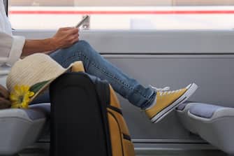 Woman traveling on train with a suitcase using smartphone