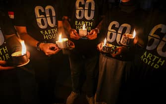 An activist hold candles during a gathering to mark the Earth Hour environmental campaign in Surabaya on March 23, 2024. (Photo by JUNI KRISWANTO / AFP)