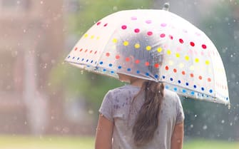 Rearview of a young girl with long brown hair holding a polka dot umbrella in the rain