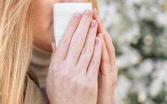 Young woman with handkerchief sneezing because of spring pollen allergy. Allergy concept