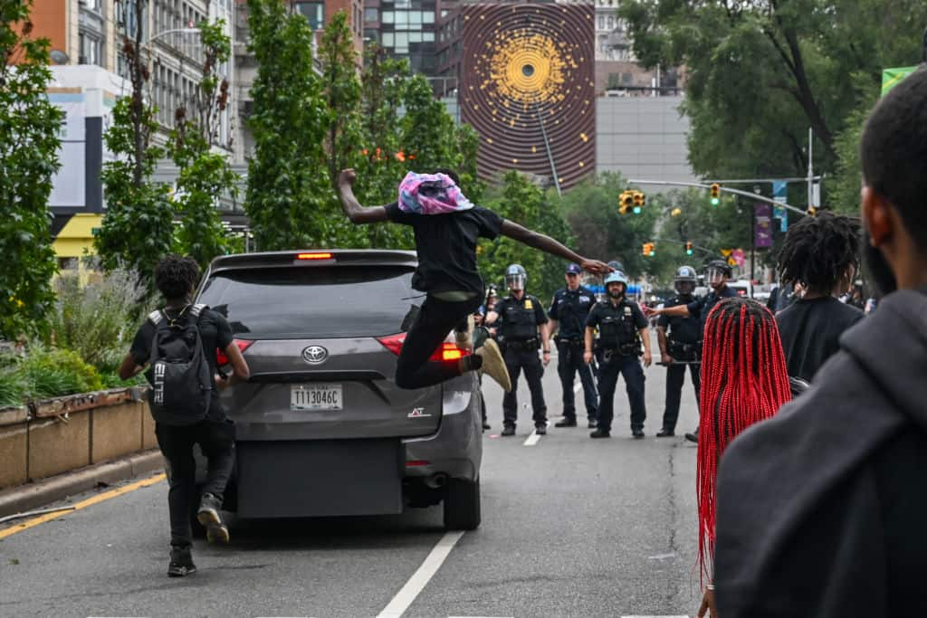 NEW YORK, NEW YORK - AUGUST 04: People kick a car as members of the NYPD respond to thousands of people gathered for a "giveaway" event announced by popular Twitch live streamer Kai Cenat in Union Square and the surrounding area on August 4, 2023 in New York City. Cenat, who announced on social media that he would be giving away video game consoles and other items, is reportedly in police custody after a crowd sparked disorder in the park leading to numerous arrests.  (Photo by Alexi J. Rosenfeld/Getty Images)