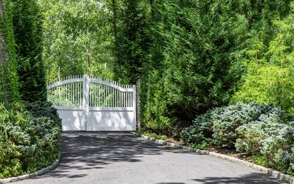 lush landscape and paved driveway with white electric gates