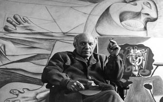 Portrait of Spanish artist Pablo Picasso (1881 - 1973) as he smokes a cigarette, seated in front of several of his paintings, Paris, France, circa 1950. (Photo by Sanford Roth/Photo Researchers History/Getty Images)