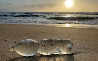 Plastic shiny bottle waste on wild sea coast, sunset time,pollution,italy