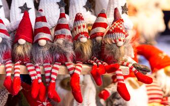 Close up color image depicting Santa's little elfin helpers Christmas decorations in a row and for sale at a Christmas market. They are sitting on a shelf and are wearing red stripy stockings and pointed hats.
