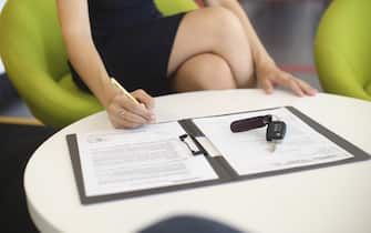 Unrecognizable female customer signing a document in a car dealership.