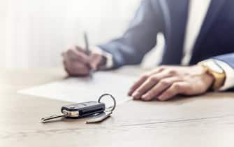 The agent signs a contract for the purchase or Leasing of a new car. New car keys in the foreground.
