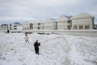 People walk by and photograph homes covered in ice at the waterfront community of Crystal Beach in Fort Erie, Ontario, Canada, on December 28, 2022, following a massive snow storm that knocked out power in the area to thousands of residents. (Photo by Cole Burston / AFP) (Photo by COLE BURSTON/AFP via Getty Images)