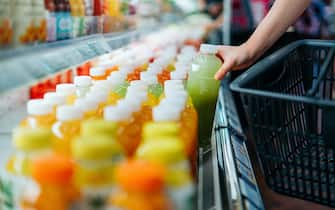 Cropped shot of young Asian woman shopping for fresh fruit juice from refrigerated shelves in supermarket, taking out a bottle of freshly squeezed green juice into a shopping basket. Healthy eating, go green lifestyle