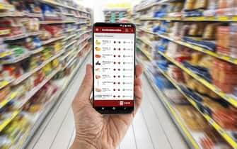 Man's hand holding a smartphone wich displays an online shopping application. In the background a supermarket lane made unrecognizable by retouching, blur and motion effect. The application layout is an original creation by the author of this image.