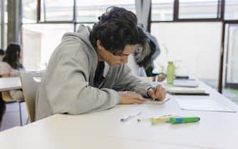 A high school student sitting at his desk and concentrating on a written assignment during class.