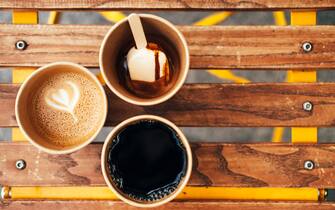 Coffee break with friends. Four disposable cups with water, cappuccino, brewed coffee and coffee with ice cream placed on wooden table. Photography from above with copy space for your design
