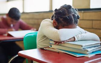 Shot of a young girl sleeping at her desk in a classroom