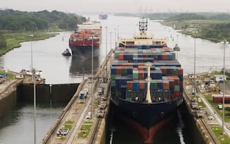 Several freighters, assisted by tugboats, are entering the Panama Canal at Gatun Locks on the Atlantic side. These container ships are fully loaded with cargo heading west towards the Pacific.