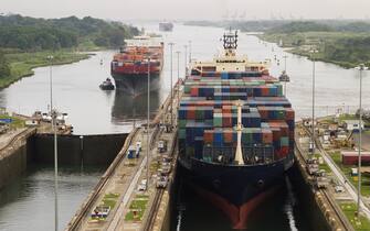 Several freighters, assisted by tugboats, are entering the Panama Canal at Gatun Locks on the Atlantic side. These container ships are fully loaded with cargo heading west towards the Pacific.