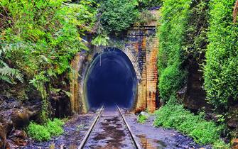 Historic railway tunnel deep into mountain surrounded by lush vegetation of rain forest in NSW. Entrace of single railway trail and brick laid portal.