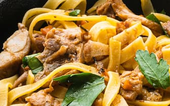 Homemade Rabbit stew pappardelle set, in frying cast iron pan or pot, on black wooden table