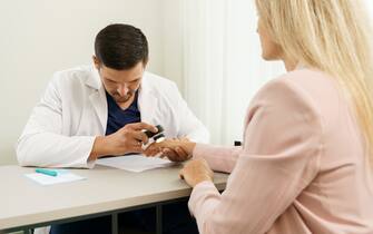 Doctor and client woman in dermatology clinic. Dermatologist is using dermatoscope for skin examination.