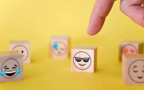 The finger points to a smiley emoji with glasses on a yellow background. The concept of the world day of emoticons.