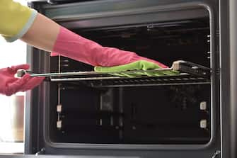 Cleaning the oven. Woman's hand in household cleaning gloves cleans oven inside. Clean oven in kitchen.