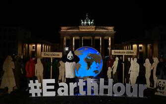Activists from WWF, one of them in a panda suit, hold placards reading "Protect the Climate" and "Strengthen Democracy" as they pose in front of Berlin's landmark the Brandenburg Gate with its lights switched on, to mark the Earth Hour environmental campaign on March 23, 2024. (Photo by John MACDOUGALL / AFP)