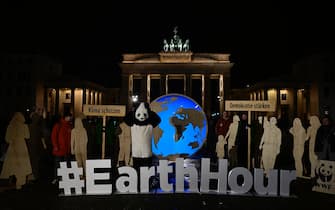 Activists from WWF, one of them in a panda suit, hold placards reading "Protect the Climate" and "Strengthen Democracy" as they pose in front of Berlin's landmark the Brandenburg Gate with its lights switched on, to mark the Earth Hour environmental campaign on March 23, 2024. (Photo by John MACDOUGALL / AFP)