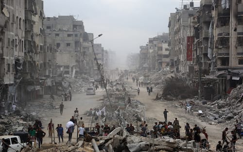 Palestinians make their way past destroyed buildings in Gaza City on October 12, 2025. Hundreds of thousands of Palestinians returned to a devastated Gaza City, after an Israel-Hamas ceasefire came into effect, and as both sides discuss implementing US President Donald Trump's 20-point plan to end the war, which calls for Hamas' disarmament and for the group not to be involved in running post-war Gaza. (Photo by Bashar TALEB / AFP)