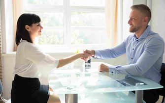 Smiling Young Businessman Shaking Hand With Female Candidate Over Desk At Workplace