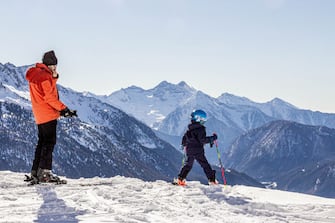 Family time on the ski slopes of Antagnod. The young kid is waiting for his father to  skiing while admiring the landscape, Valle d'Aosta, Italy, Europe. (Photo by: Fabio Enrico ViganÃ²/REDA&CO/Universal Images Group via Getty Images)