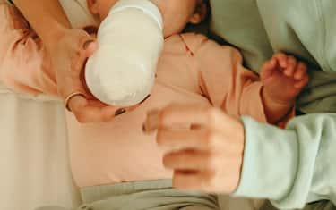 Overhead view of a loving mother feeding her newborn baby. High angle view of a new mom giving her baby formula milk while lying on the bed. Single mo