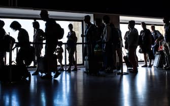 Silhouettes of passengers standing in line inside Aeropuerto de Sevilla, España, with luggage and carry-on bags, waiting for their boarding call.