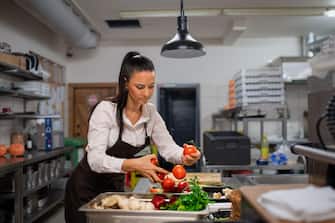 Professional female chef cutting vegetables indoors in restaurant kitchen.